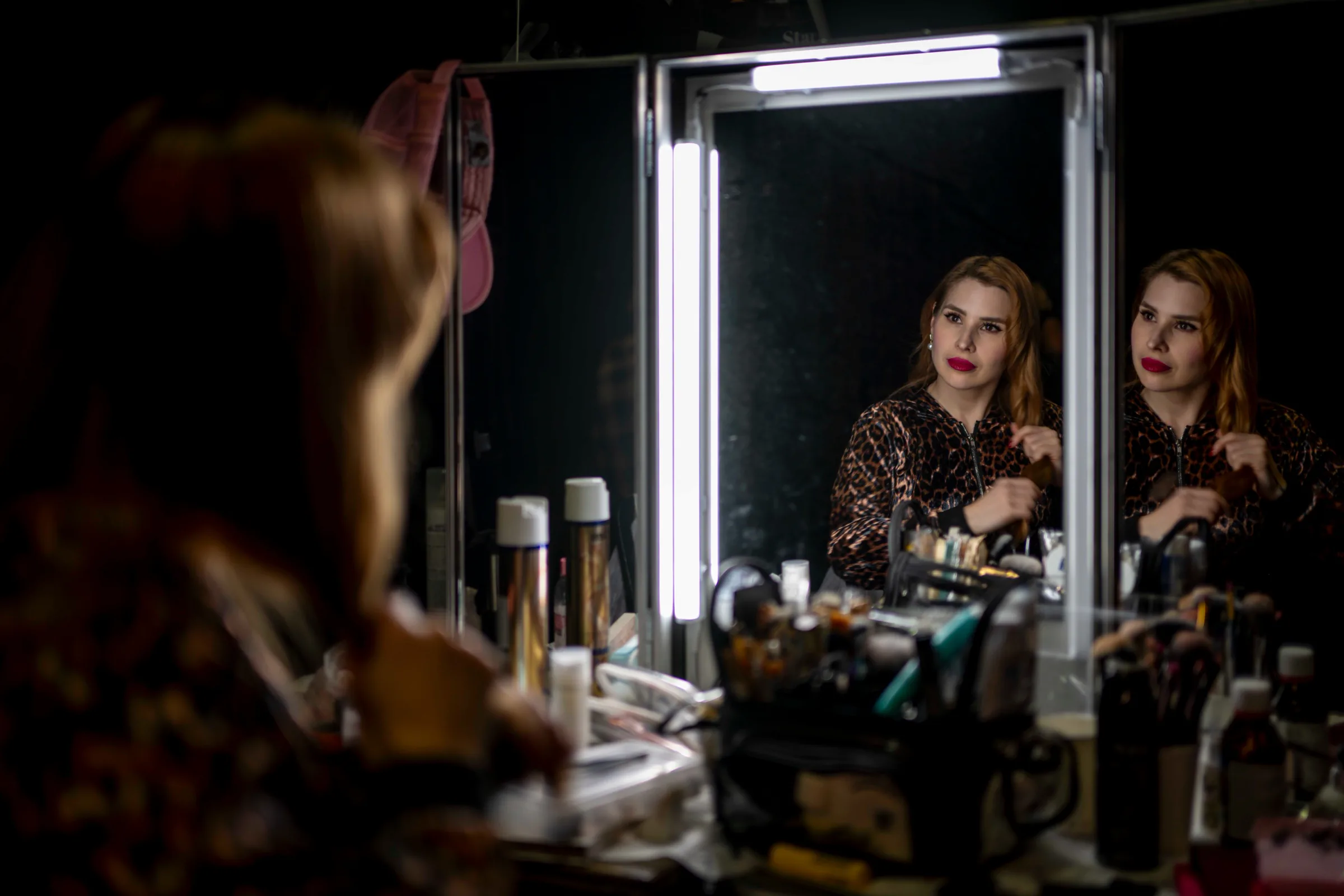 A performer checking her reflection at the lit dressing-room mirror