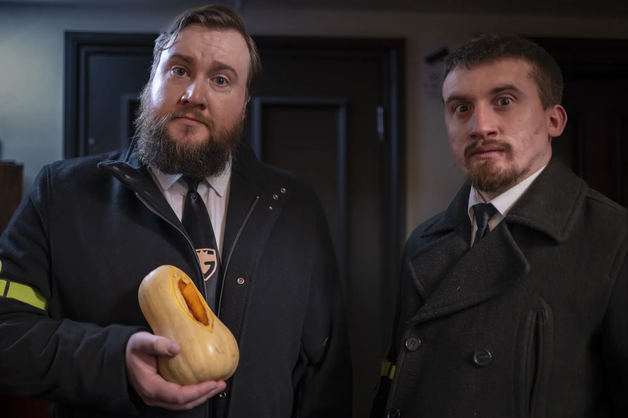 Two men in dark overcoats at the club door, one holding a butternut squash