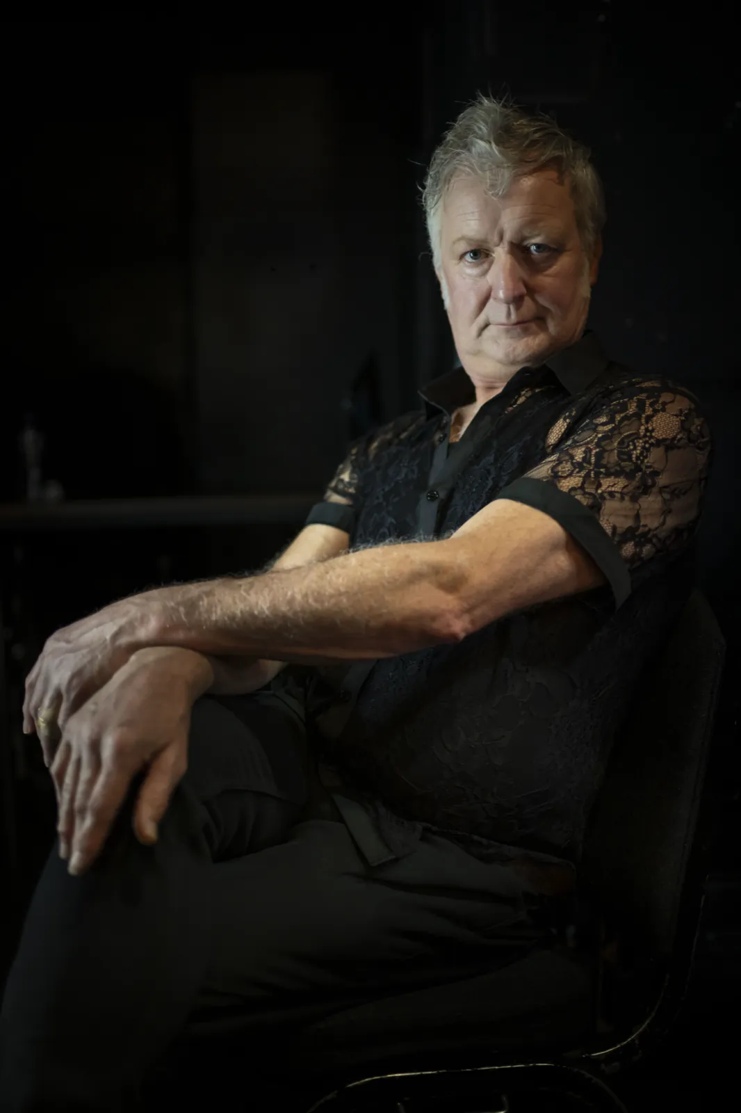 A man in a black lace shirt seated in the darkened club
